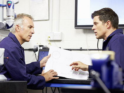 Two Engineers Discussing Plans With CMM Arm In Foreground